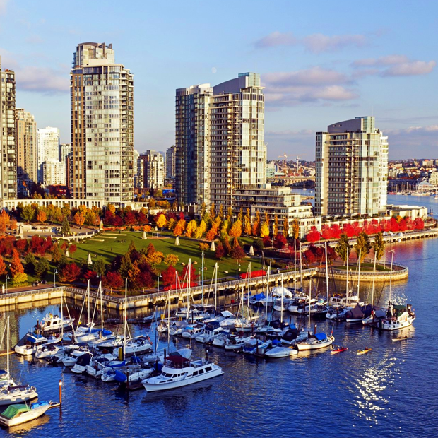 Aerial view of a coastal city skyline with marina and green parkland under blue sky